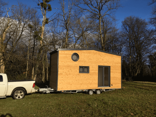 Tiny house de Damien tirée par une voiture. Sur une remorque 6.6 m, toiture 2 pans avec un bel œil de bœuf.